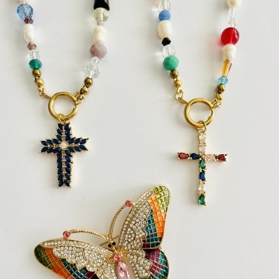 Dois colares coloridos com pendentes de cruz e um broche de borboleta colorido com pedras