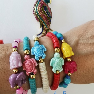Cinco pulseiras coloridas com contas e pingentes de animais e Buda sobre pulso com fundo branco e ornamento de papagaio