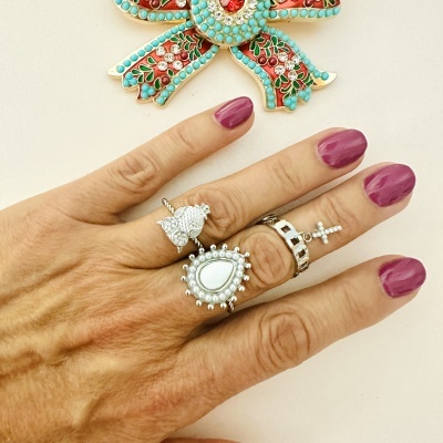 Mão com três anéis prateados detalhados e broche decorativo colorido