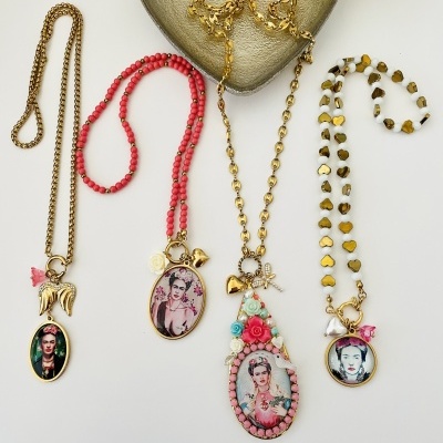 Quatro colares com pendentes de Frida Kahlo em diferentes correntes e decorações sobre fundo branco e objetos decorativos.