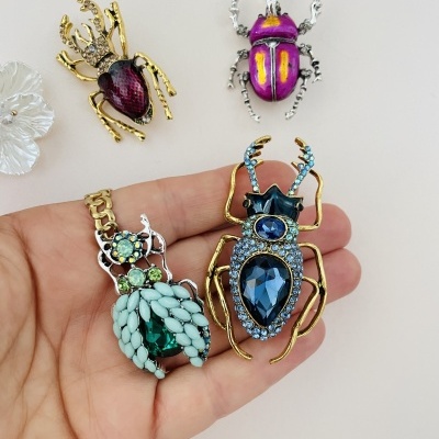Broches decorativos de insetos com pedras coloridas numa mão sobre fundo claro