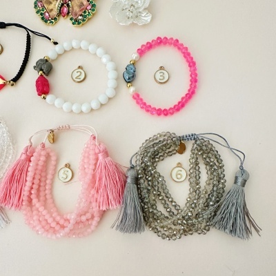 Pulseiras coloridas com contas e tasséis, numeradas de 2 a 6 sobre fundo claro