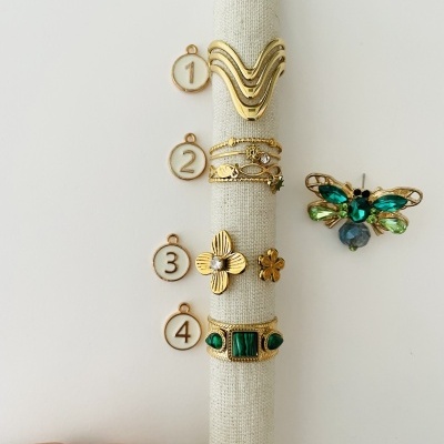 Conjunto de anéis dourados numerados com pedras verdes e broche em forma de abelha com pedras brilhantes