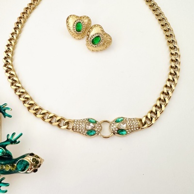 Colar e brincos dourados com pedras verdes e brancas sobre fundo branco.