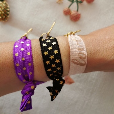 Três pulseiras coloridas de tecido com padrões dourados num pulso sobre fundo claro