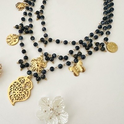 Colar com contas pretas e pendentes dourados variados sobre fundo branco