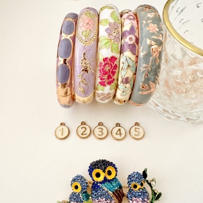 Pulseiras esmaltadas florais, medalhas numeradas e broche de corujas colorido