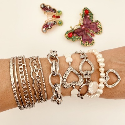 Pulsera variada com correntes, pérolas e corações, com broches de borboleta e libélula ao fundo