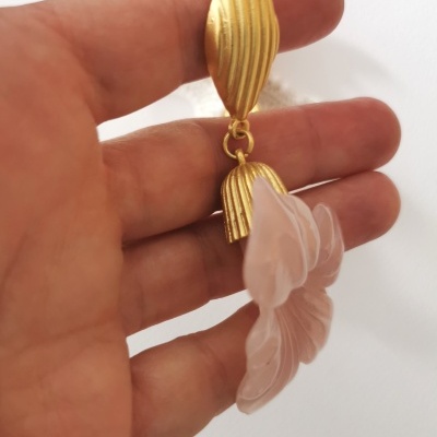 Brinco dourado com pendente de vidro fosco sendo segurado por uma mão.