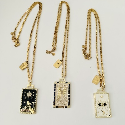 Três colares dourados com pendentes retangulares decorados com símbolos e texto SACRED HEALS