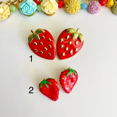 Dois pares de brincos morango vermelho com detalhes dourados e corrente dourada com flores coloridas ao fundo