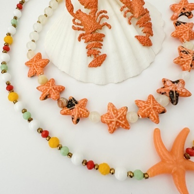 Conjunto de bijuteria com lagostas e estrelas-do-mar de cor laranja sobre concha branca