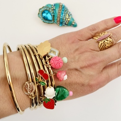 Pulseiras douradas com pendentes coloridos em mão feminina com anel rosa