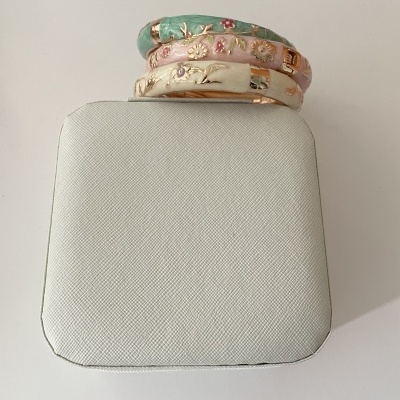 Três pulseiras esmaltadas com detalhes florais sobre caixa branca texturizada