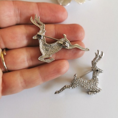Dois broches prateados em forma de cervo saltando com pedras brilhantes em fundo branco