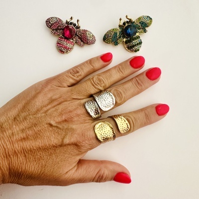Mão com anéis texturizados e dois broches em forma de abelha com pedras coloridas