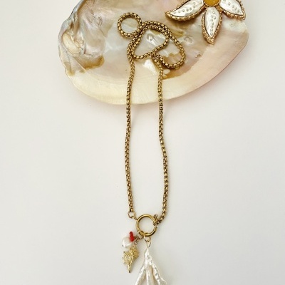 Colar dourado com pendentes de coral branco sobre concha nacarada decorada com broche de flor.