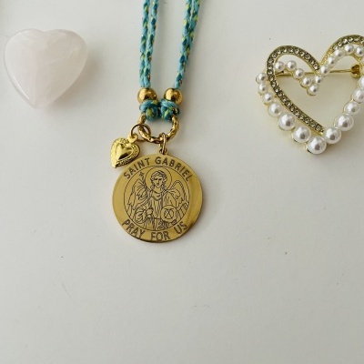 Colar dourado de São Gabriel com cordão azul e detalhes em dourado, colocado com corações decorativos