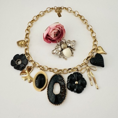 Colar dourado com pendentes de flores e corações, broche tipo besouro com cristais e preto e branco, fundo branco