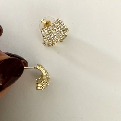 Par de brincos dourados em meia-lua com pedras brilhantes sobre fundo branco