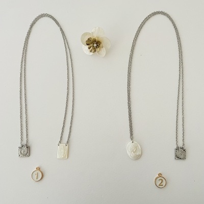 Dois colares prateados com pendentes religiosos e medalhas numeradas sobre fundo branco