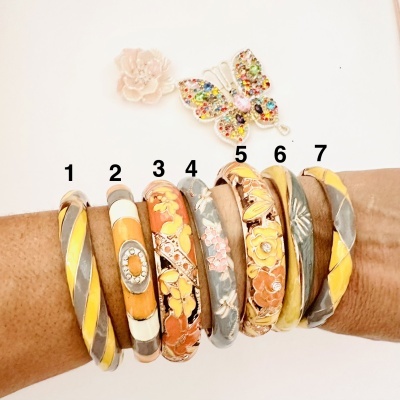 Conjunto de sete pulseiras metálicas coloridas com padrões florais e texturas diversas num braço.