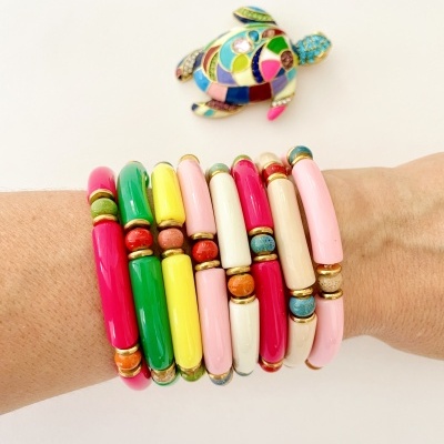 Pulseiras coloridas em segmentos lisos e contas redondas com elásticos dourados, com tartaruga decorativa multicolorida ao fundo