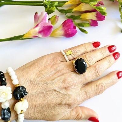 Mão feminina com anéis e pulseiras coloridas, flores ao fundo