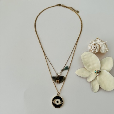 Colar dourado com pingentes variados sobre superfície branca com flor e concha ao lado.