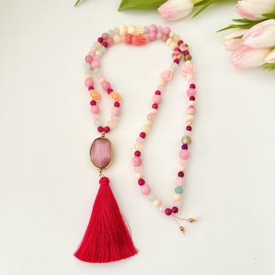 Colar colorido com pendente oval rosa e tassel vermelho sobre fundo branco e tulipas rosas