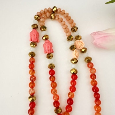Colar colorido com contas laranja, douradas, cabeça de Buda e flores sobre fundo branco.