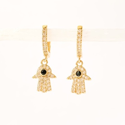Brincos dourados em forma de mão com pedras brilhantes e uma pedra preta no centro