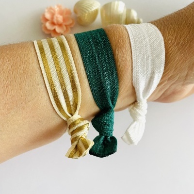 Três pulseiras de tecido elástico em pulso com conchas e flor ao fundo