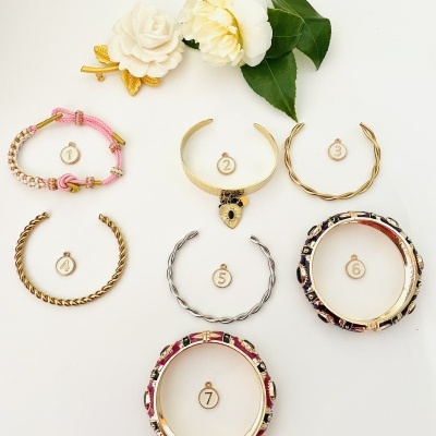 Sete pulseiras variadas e duas flores brancas com folhas verdes em fundo branco