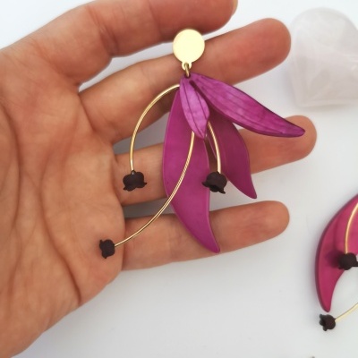 Brinco decorativo roxo com flores negras e metal dourado na mão