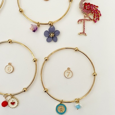 Três pulseiras douradas com pingentes e broche flamingo rosa