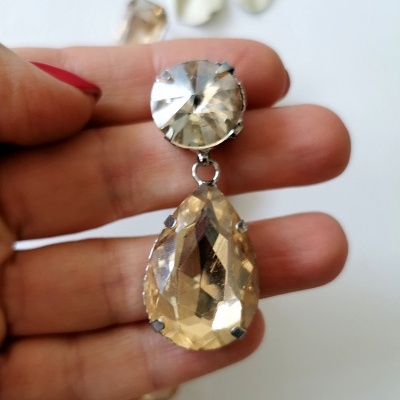 Brinco com cristais transparente e amarelo segurado por mão com unhas vermelhas