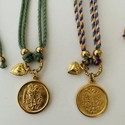 Dois colares com medalhões dourados em cordões trançados, um verde e outro colorido