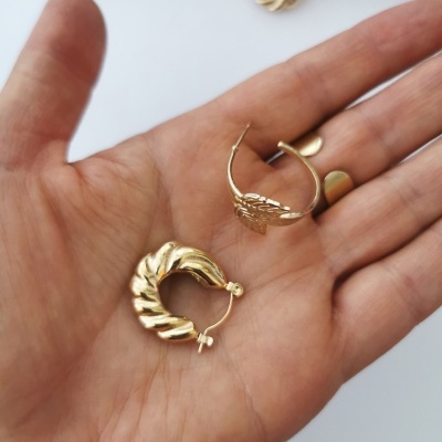 Brincos dourados tipo argola com textura ondulada numa mão
