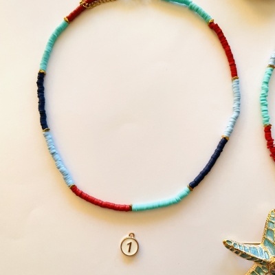 Colar colorido azul e vermelho com pingente número 1 num fundo claro com acessórios dourados.