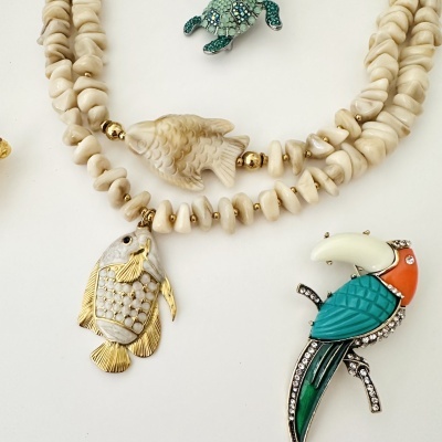 Bijuterias variadas com colares de contas e pingentes de peixes, broche de tartaruga verde e broche de pássaro colorido