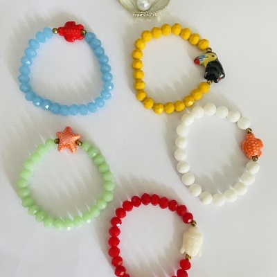 Pulseiras coloridas com contas e pingentes de animais, ao lado de uma caixinha prateada em formato de concha com pérola