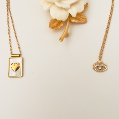 Dois colares dourados com pendentes diferentes e uma rosa decorativa branca com folhas douradas