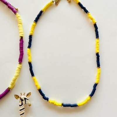 Colar amarelo e azul com fecho dourado, pendente girafa e colar amarelo e roxo em fundo branco