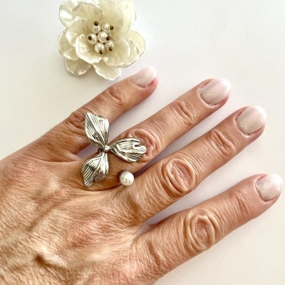 Anel prateado com pérola e flor decorativa branca em fundo branco