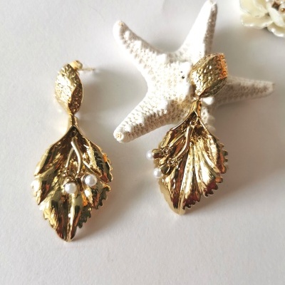 Brincos dourados em forma de folha com pérolas, estrela-do-mar e decoração branca ao fundo