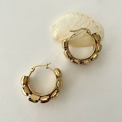 Brincos de argola dourados com textura segmentada numa superfície branca com uma concha