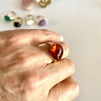 Mão com anel âmbar e outros anéis coloridos desfocados no fundo