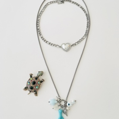 Colar e pulseira prateados com pendentes marinhos e broche de tartaruga com pedras coloridas sobre fundo branco