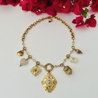 Colar dourado com pendentes variados e flores vermelhas ao fundo